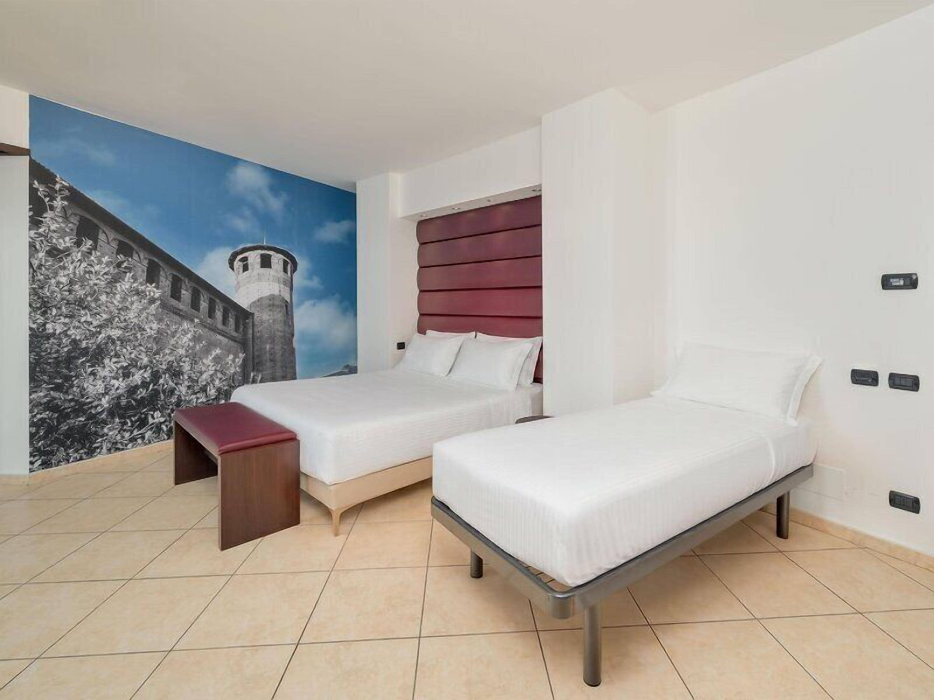 Une chambre d’hôtel avec deux lits, une fresque représentant un château et un banc rouge.