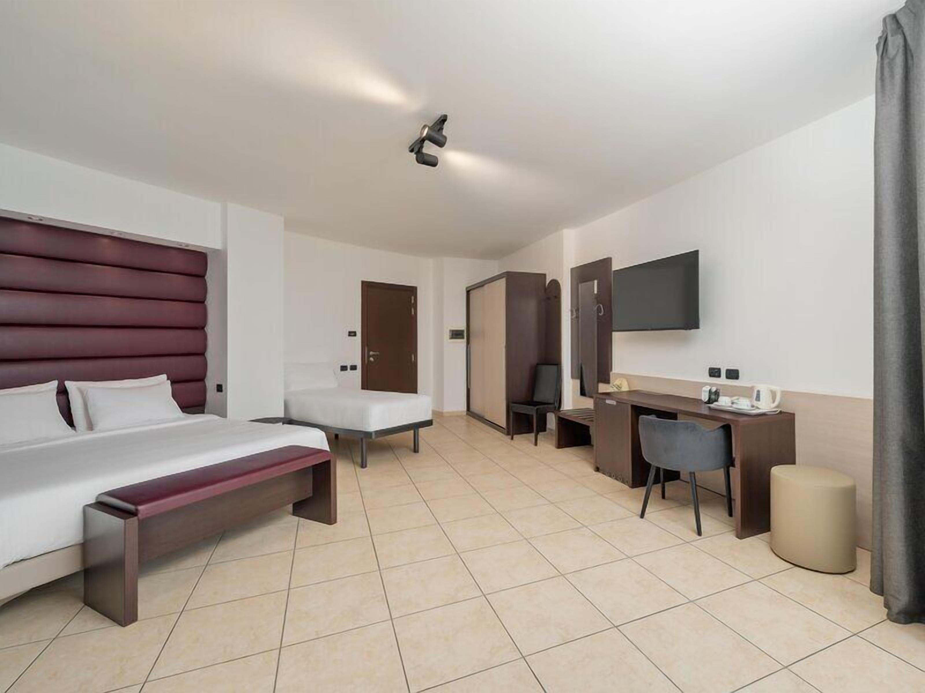 A hotel room with a bed, a desk, a chair, a TV, and a wardrobe.