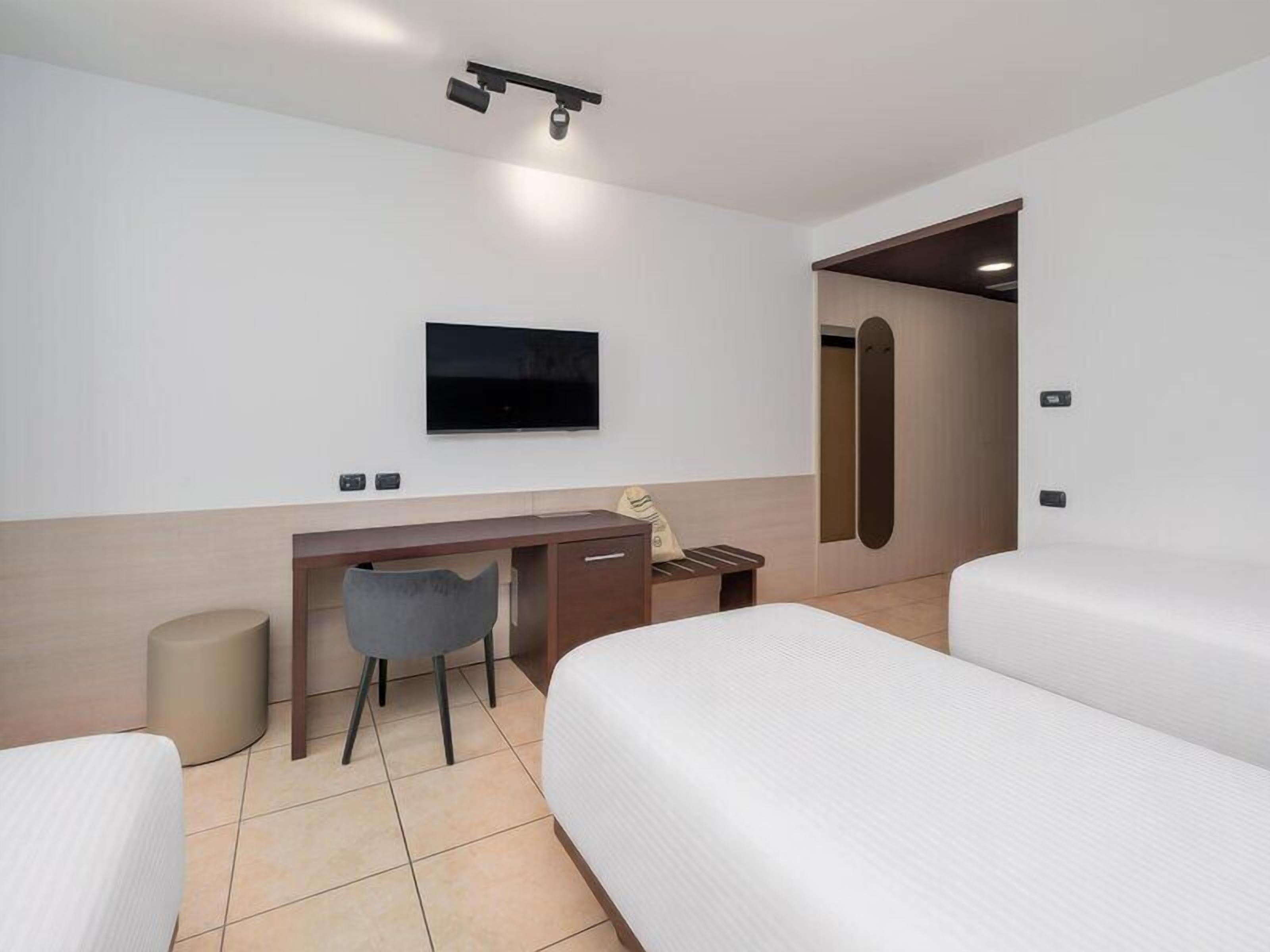 A hotel room with a bed, a desk, a chair, a TV, and a door.