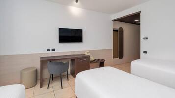 Una camera d'albergo con un letto, una scrivania, una sedia, una televisione e una porta.