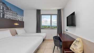 A hotel room with two beds, a desk, a chair, a TV, and a window with a view.