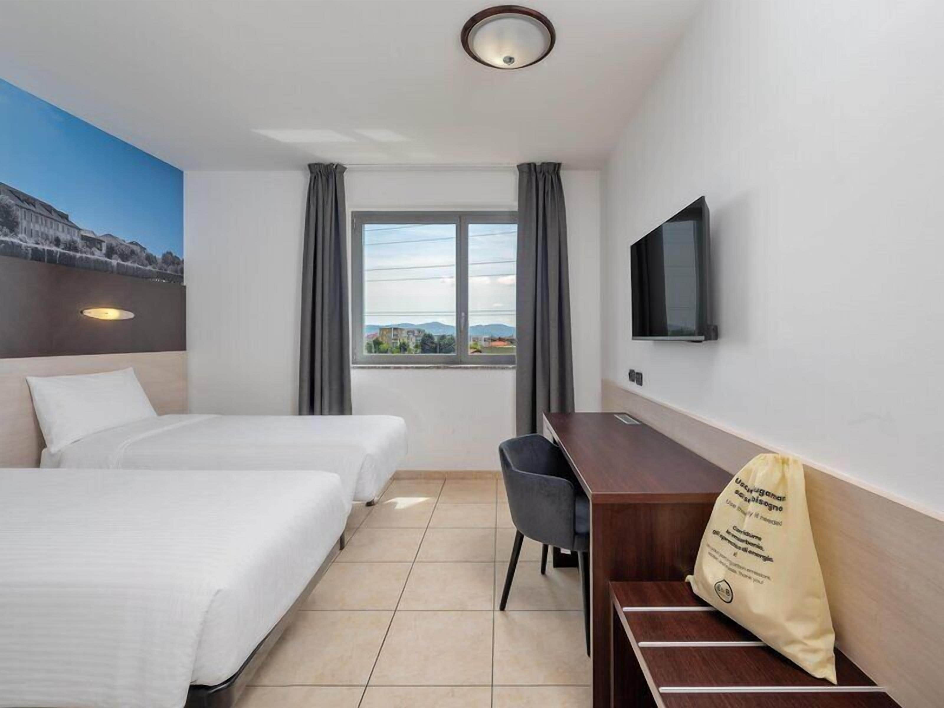 Een hotelkamer met twee bedden, een bureau, een stoel, een televisie en een raam met gordijnen.