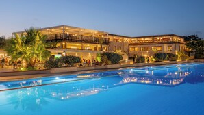 A hotel with a large outdoor swimming pool, multiple balconies, and well-lit outdoor areas. - VOI Tanka Village (Villasimius)