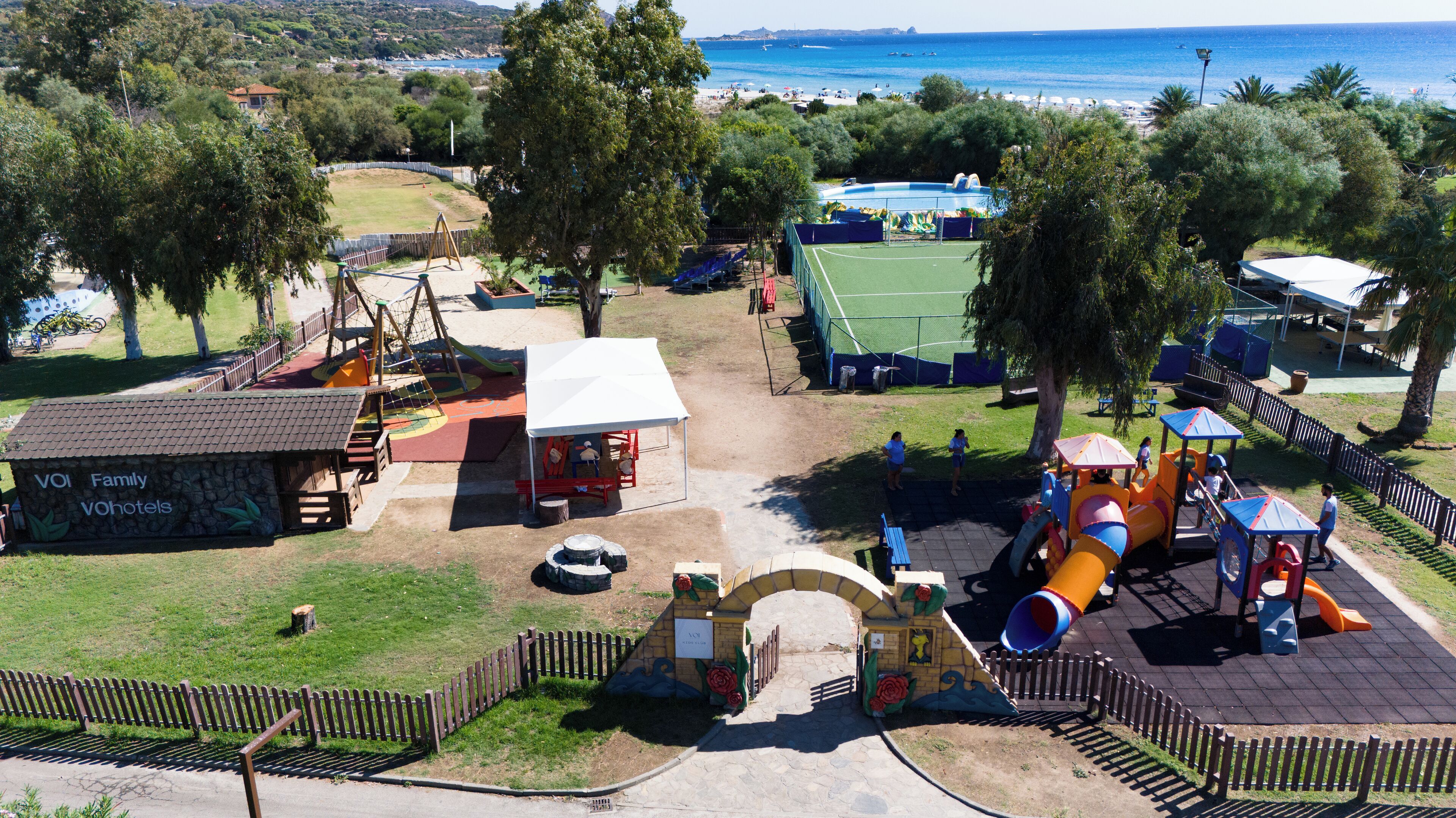 Un terrain de jeux avec des toboggans et des balançoires, un court de tennis et un bâtiment portant l’inscription « VOI Family Vohotels ».