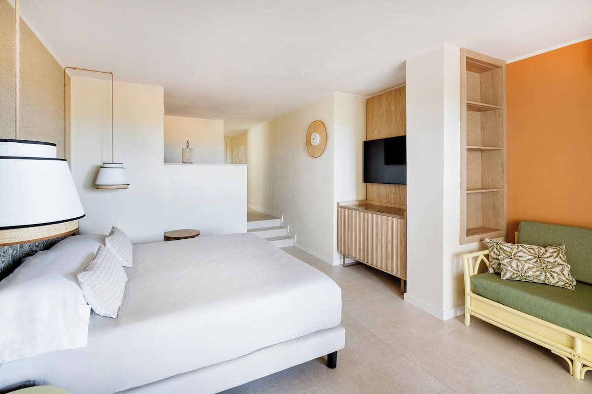 A modern hotel room with a large bed, a sofa, a TV, and a wooden cabinet.