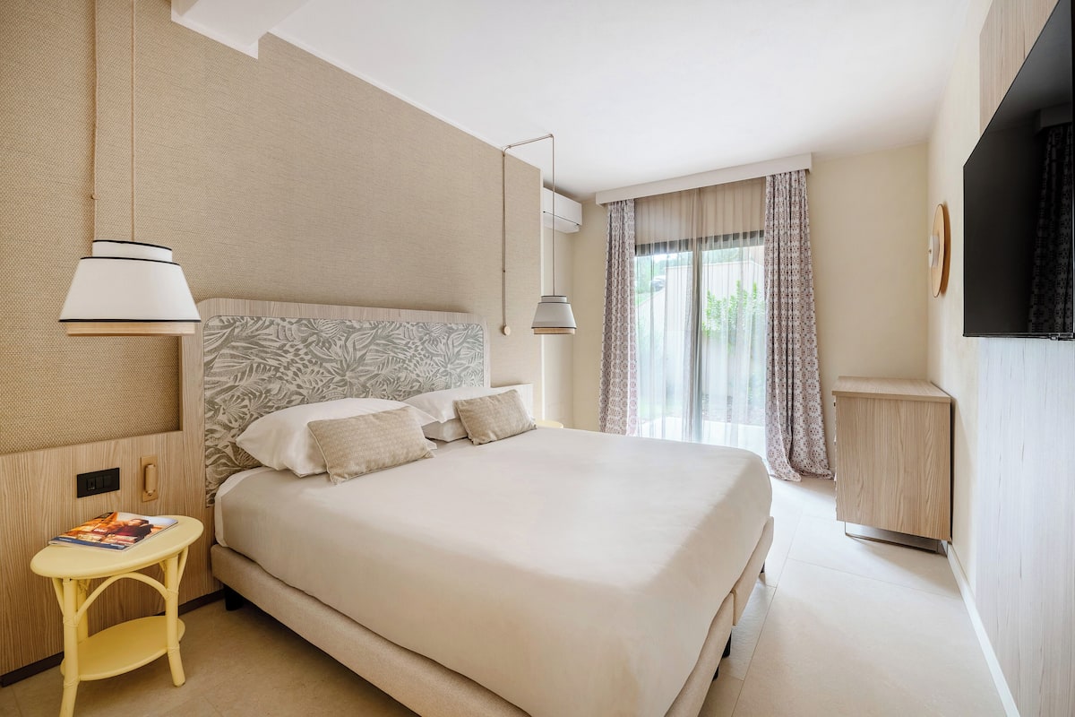 A hotel room with a large bed, a bedside table with a magazine, a lamp, and a TV mounted on the wall.
