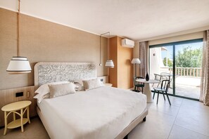 A hotel room with a large bed, a small table, a chair, and a balcony with outdoor seating. - VOI Tanka Village (Villasimius)
