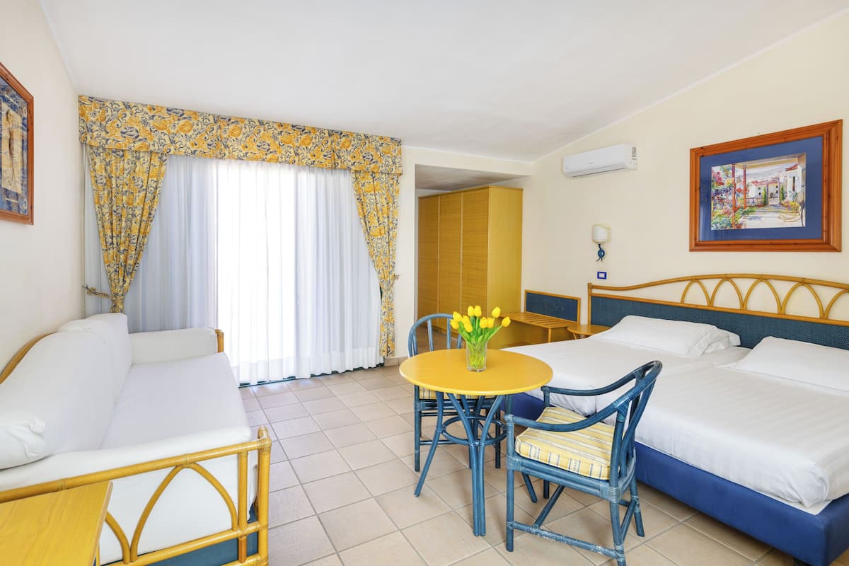 A hotel room with a bed, a sofa, a dining table with chairs, and a window with curtains.
