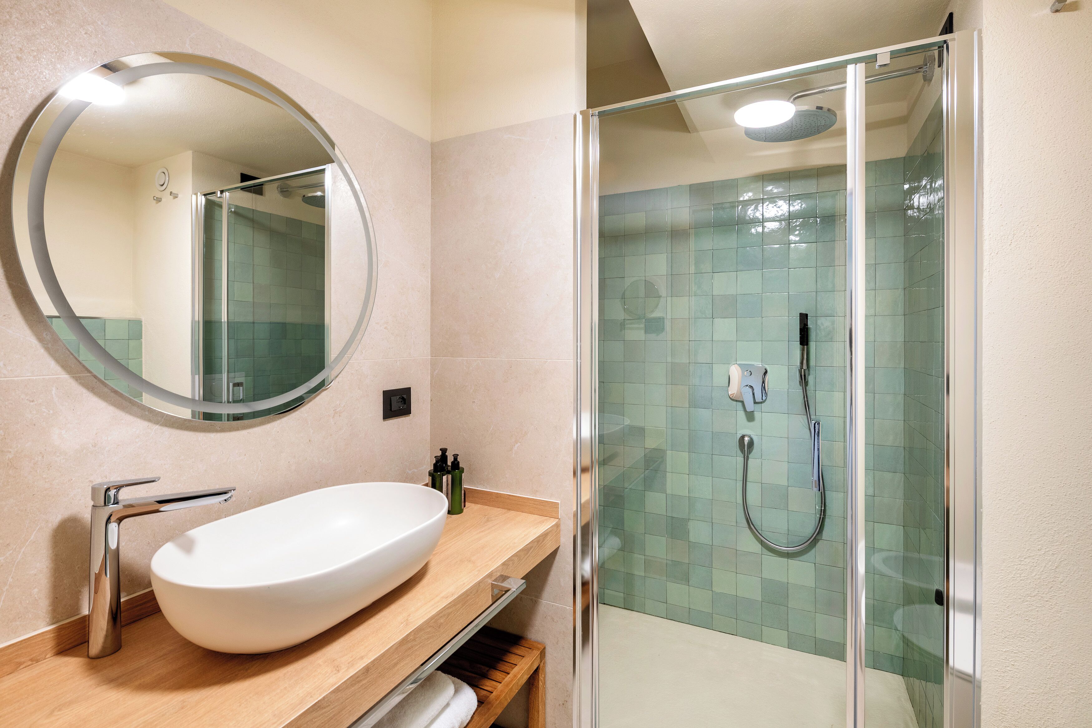 Un baño con un espejo redondo, un lavabo blanco y una zona de ducha con mampara de vidrio.