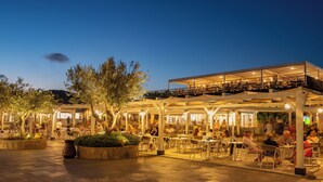 An outdoor cafe with tables and chairs, surrounded by trees and a covered seating area. - VOI Tanka Village (Villasimius)