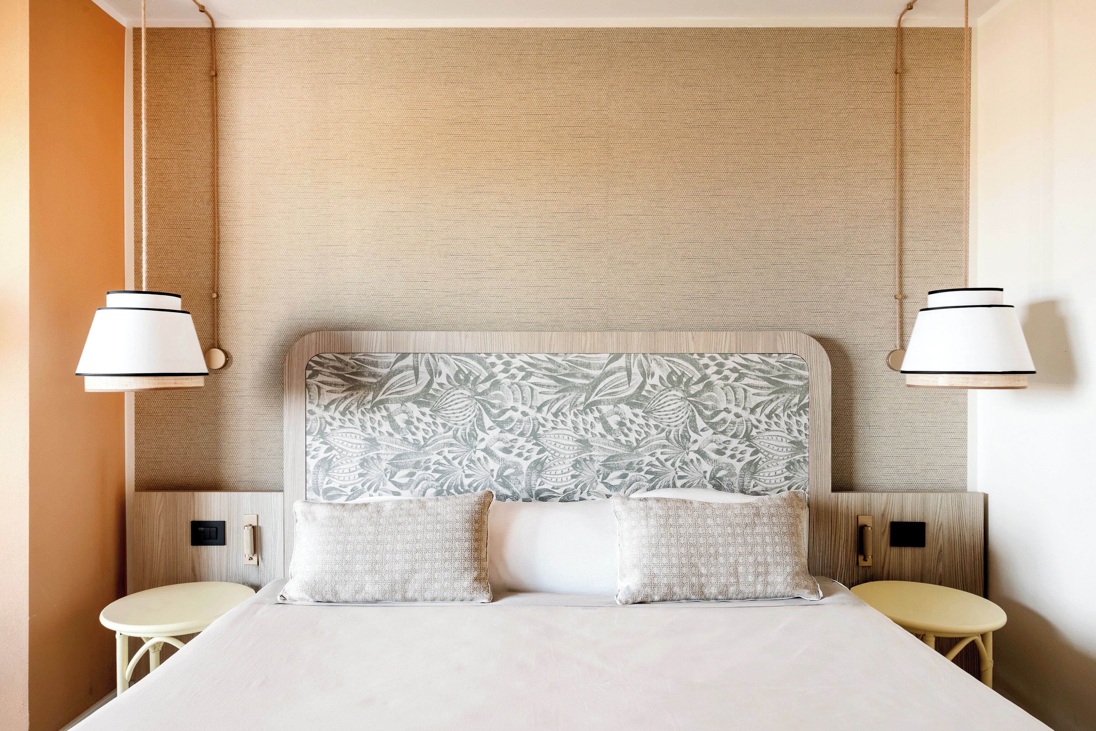 Quarto de hotel com cama grande, duas mesas de cabeceira e cabeceira com padrão de folha.