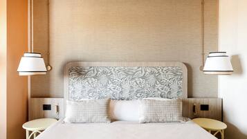 Quarto de hotel com cama grande, duas mesas de cabeceira e cabeceira com padrão de folha.
