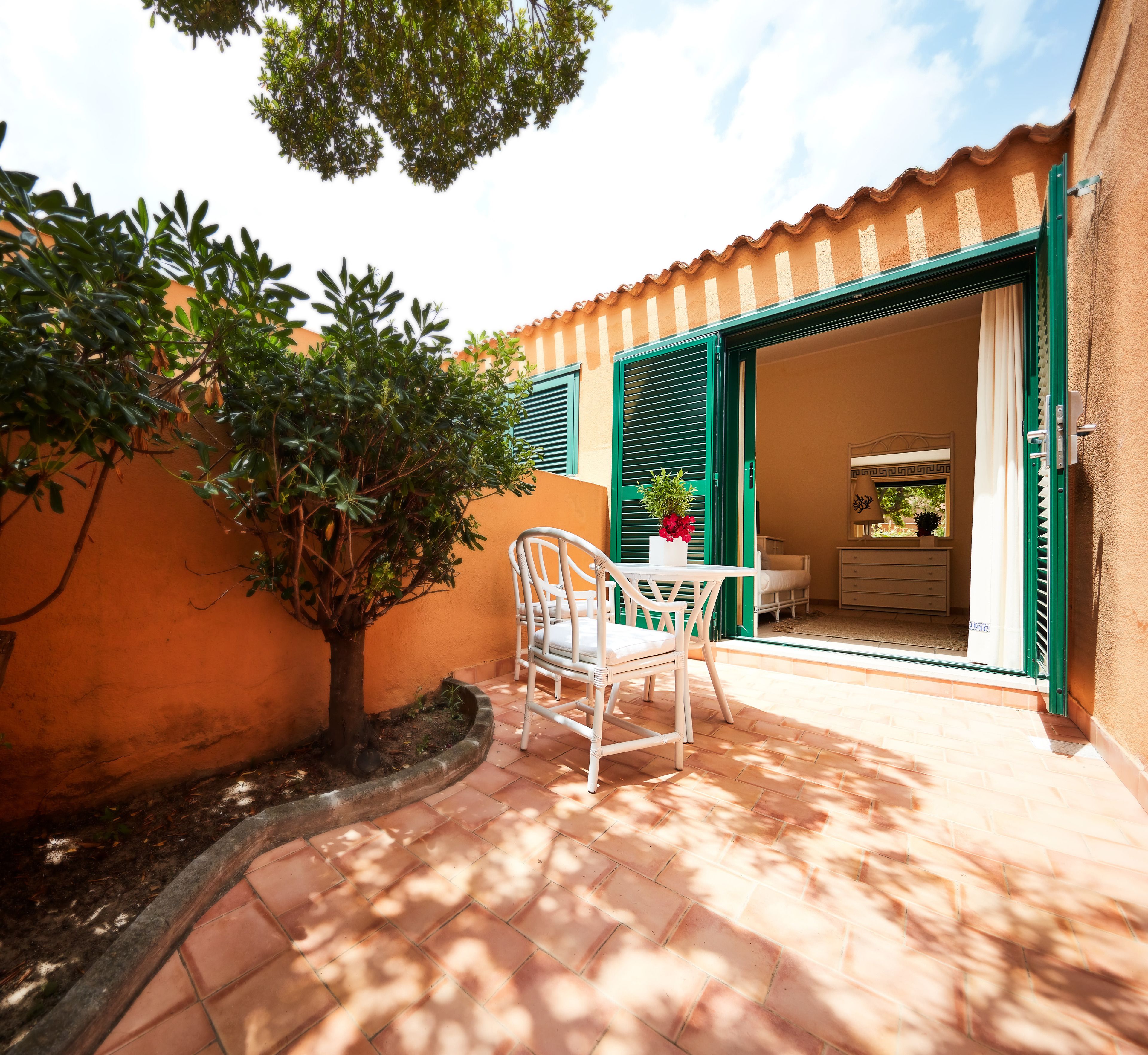 A patio with a white chair and table, a potted plant, and a door leading to an interior space.