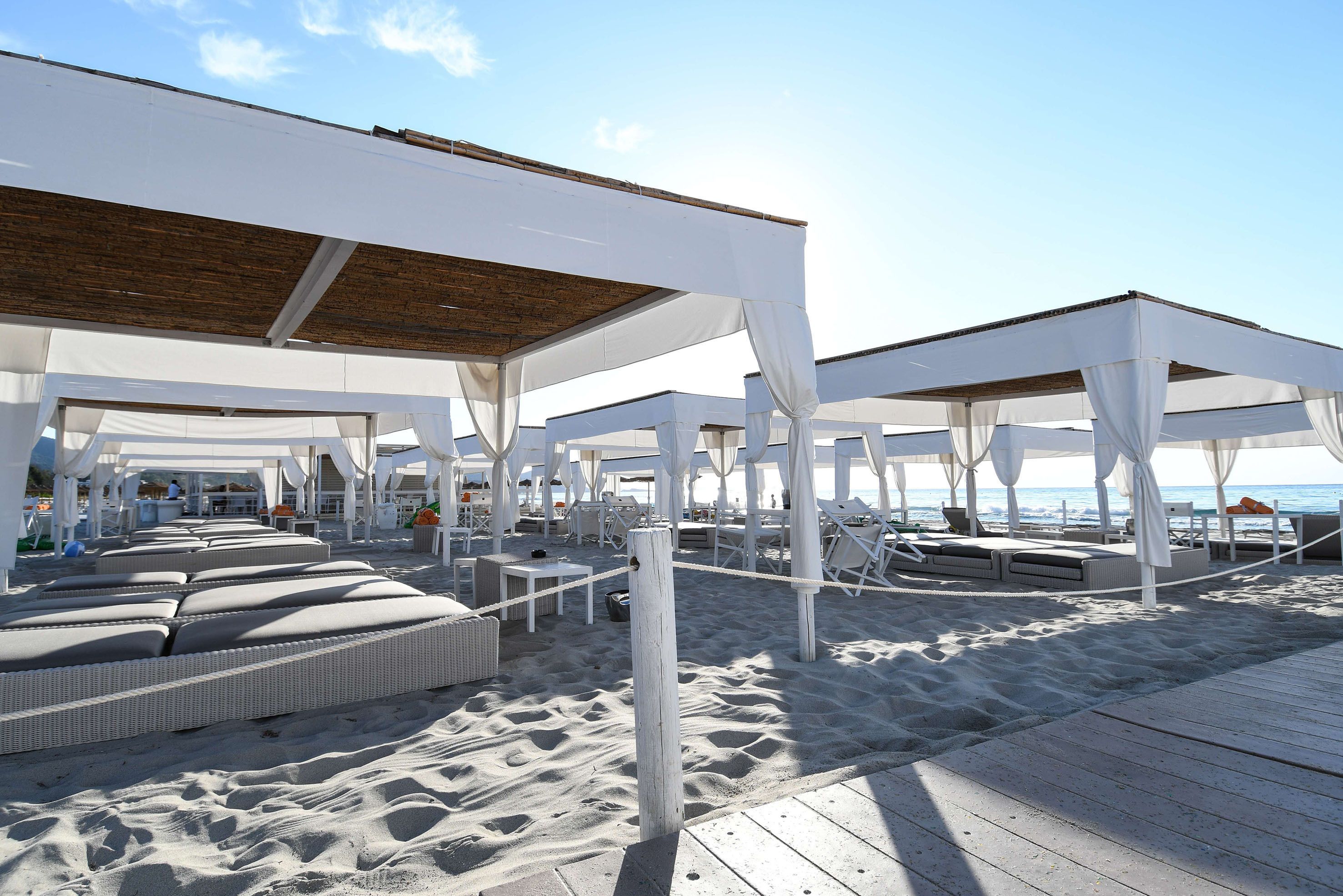 A beachside lounge area with white canopies, wicker lounge chairs, and a wooden deck.