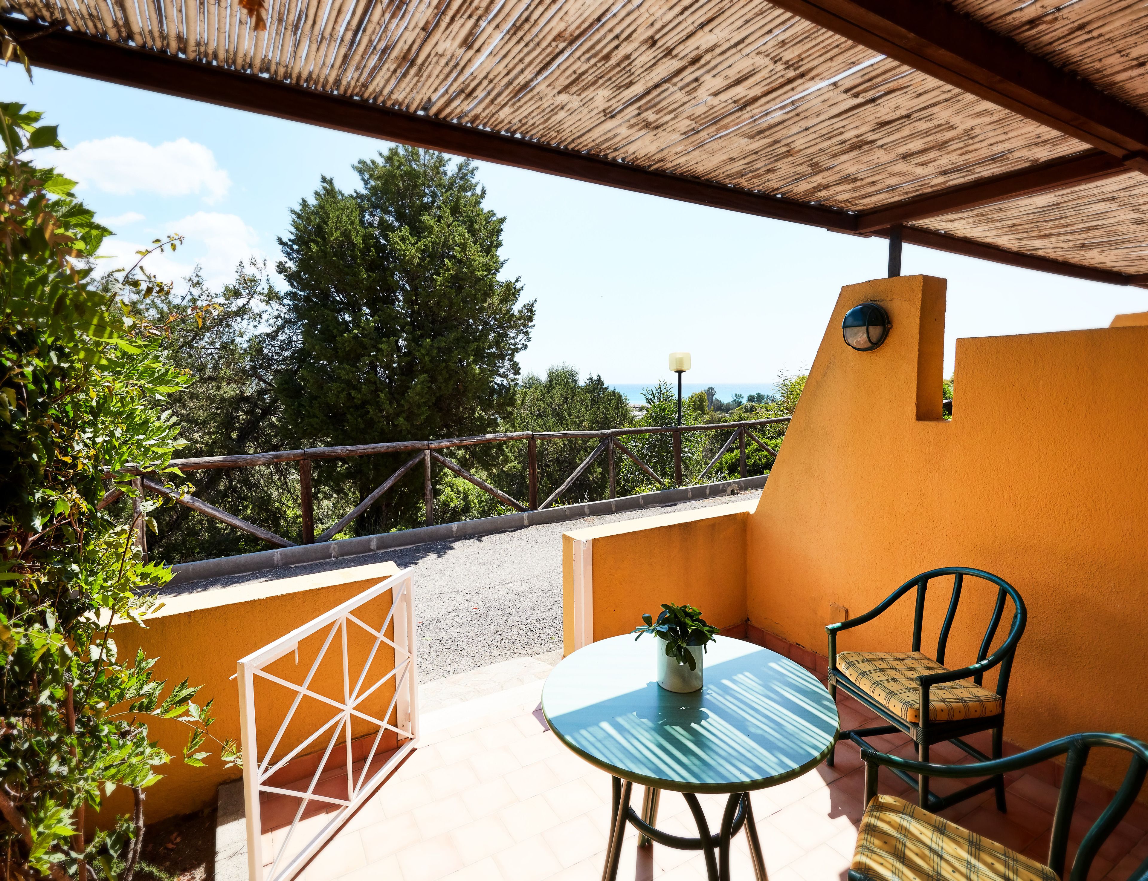 Un espace extérieur abrité, avec une table et des chaises, une plante en pot et une vue sur la mer.