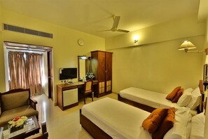 Une chambre d’hôtel équipée d’un bureau, de deux lits, d’une chaise, d’une télévision, d’une armoire et d’un ventilateur de plafond.