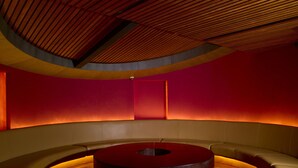 A circular seating area with a central table, surrounded by cushioned seating, in a room with curved walls and a wooden ceiling. - Grand Hotel (Kanayannur)