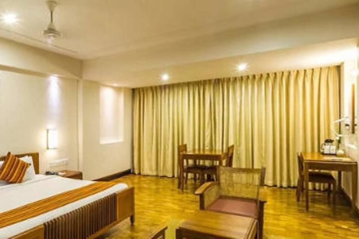 A hotel room with a large bed, a desk, a chair, and a dining table.