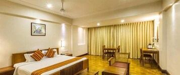 A hotel room with a large bed, a desk, a chair, and a dining table.