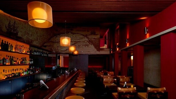 A bar area with a long counter, stools, and hanging lamps. - Grand Hotel (Kanayannur)