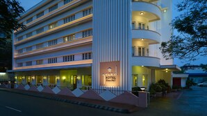 A multi-story hotel with a prominent vertical column, multiple balconies, and a well-lit entrance. - Grand Hotel (Kanayannur)