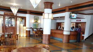 A lobby with wooden furniture, a reception desk, and a map on the wall. - Grand Hotel (Kanayannur)