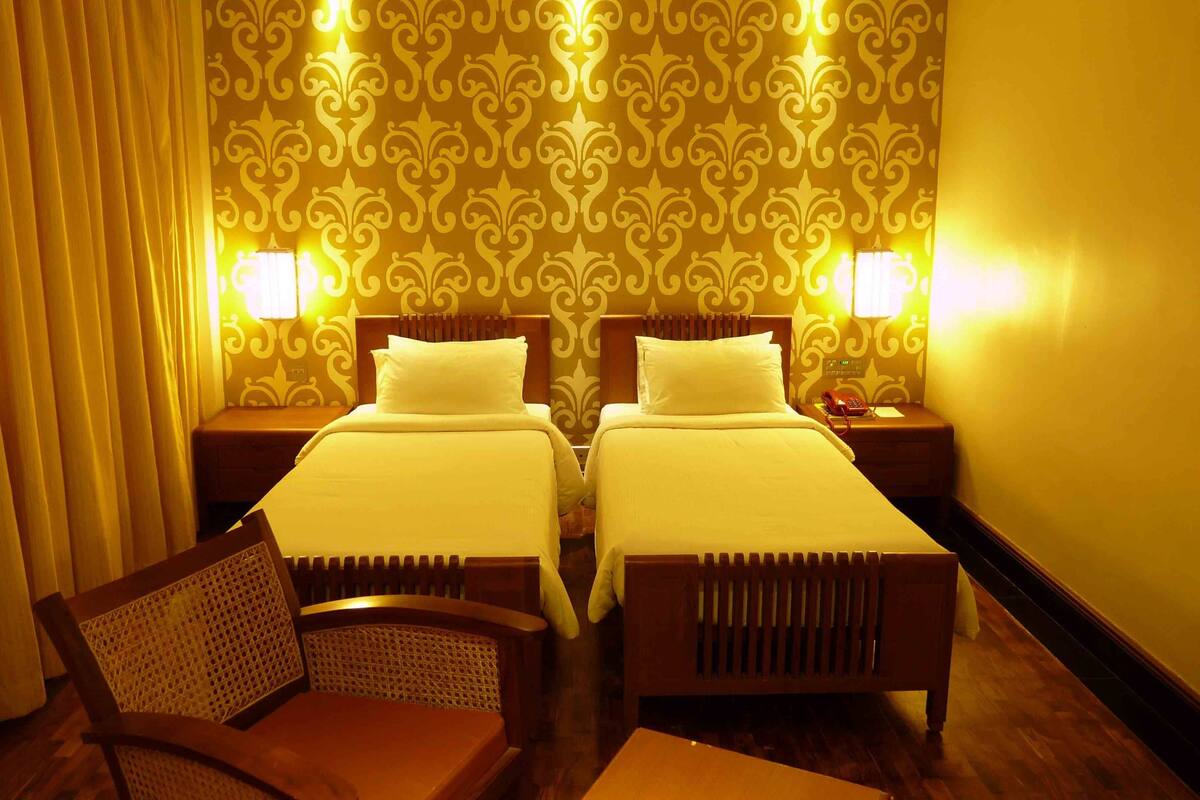 A hotel room with two beds, a wooden chair, and a nightstand with a telephone.