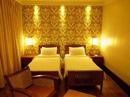 A hotel room with two beds, a wooden chair, and a nightstand with a telephone.