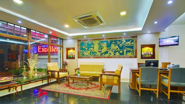 A hotel lobby with a sofa, chairs, a coffee table, a TV, and a large decorative wall piece. - Hotel Excellency (Kanayannur)