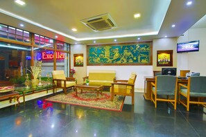 Un hall de hotel con un sofá, sillas, una mesa de centro, un televisor y un gran elemento decorativo en la pared.