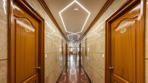 A hallway with wooden doors, numbered 212, and a geometric light fixture on the ceiling. - Hotel Excellency (Kanayannur)
