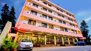 A multi-story hotel with a pink facade, multiple balconies, and air conditioning units. - Hotel Excellency (Kanayannur)