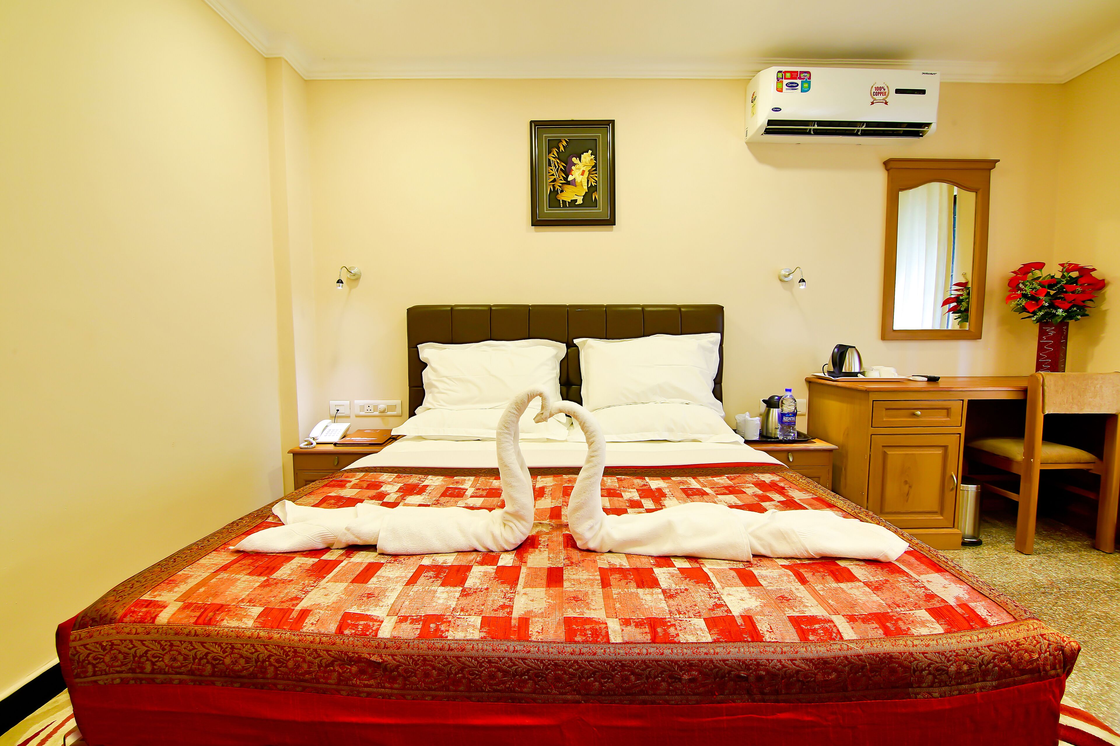 A hotel room with a bed, a nightstand, a desk, a mirror, and a wall-mounted air conditioner.