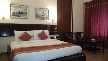 Une chambre d’hôtel avec un grand lit, deux tableaux accrochés au mur, une tête de lit en bois, un rideau rouge et une petite table avec une chaise.