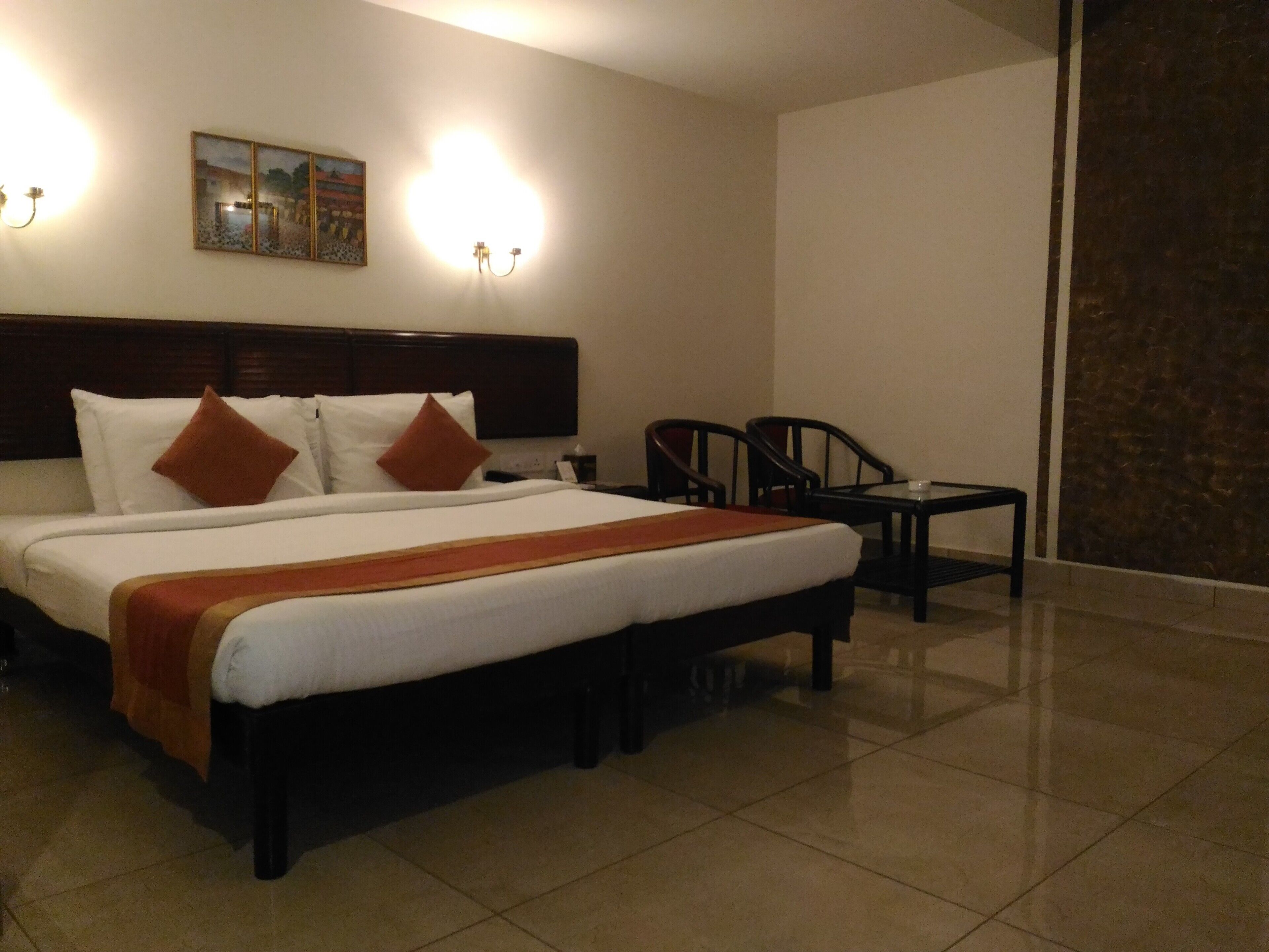 A hotel room with a large bed, two chairs, a small table, and a painting on the wall.
