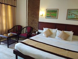 Habitación de hotel con cama, dos sillas, una mesita y dos cuadros en la pared.