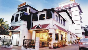 A multi-story hotel with a traditional architectural style, featuring a prominent entrance with a staircase and a signboard above. - Yuvarani Residency (Kanayannur)