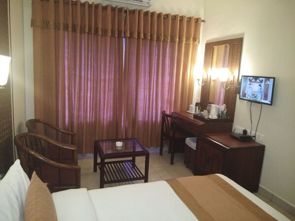 Habitación de hotel con cama, escritorio, silla, una mesita con una vela y un televisor en la pared.