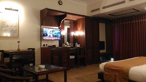 A hotel room with a bed, a desk with a chair, a television, and a small table. - Yuvarani Residency (Kanayannur)