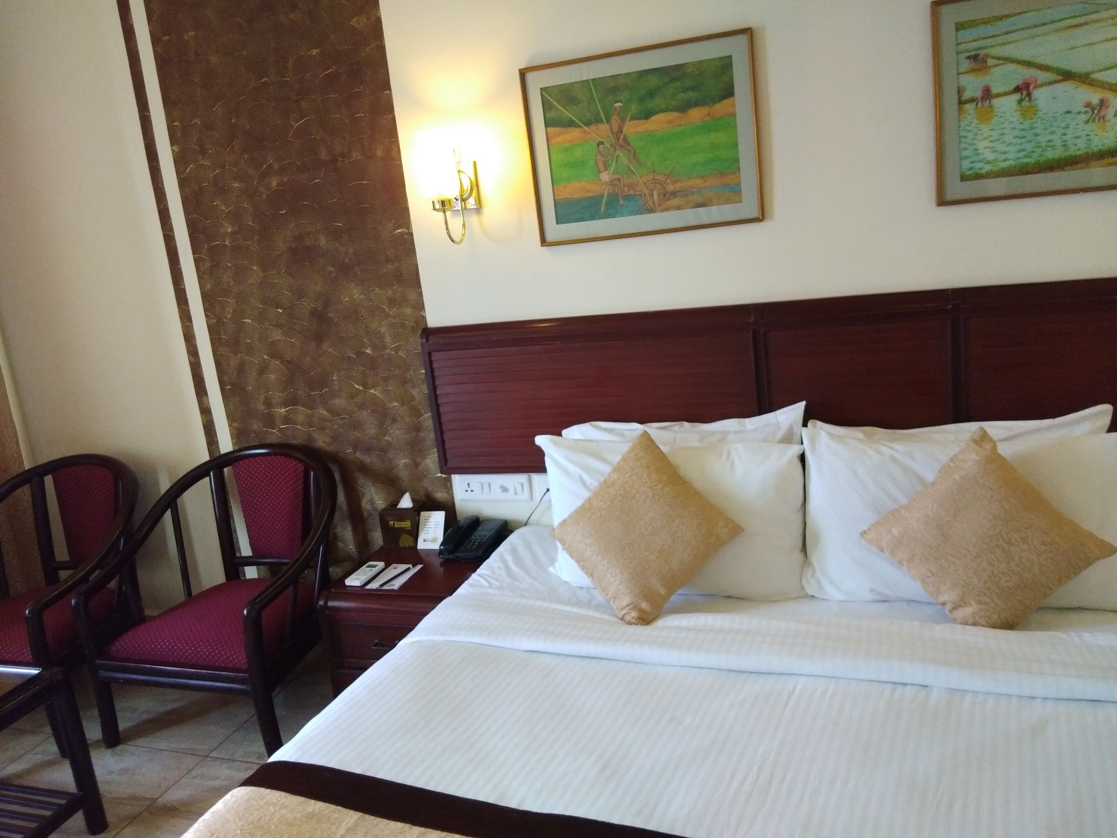 A hotel room with a large bed, a wooden headboard, two wall-mounted lamps, and two paintings.
