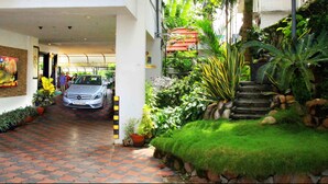 A reception area with a car parked in the background, surrounded by lush greenery and potted plants. - Yuvarani Residency (Kanayannur)
