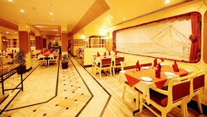 A restaurant with multiple dining tables and chairs, a patterned floor, and a large window with a view. - Yuvarani Residency (Kanayannur)