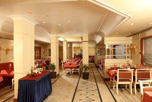 Un comedor de hotel con varias mesas y sillas, un largo pasillo y un amplio ventanal con cortinas.