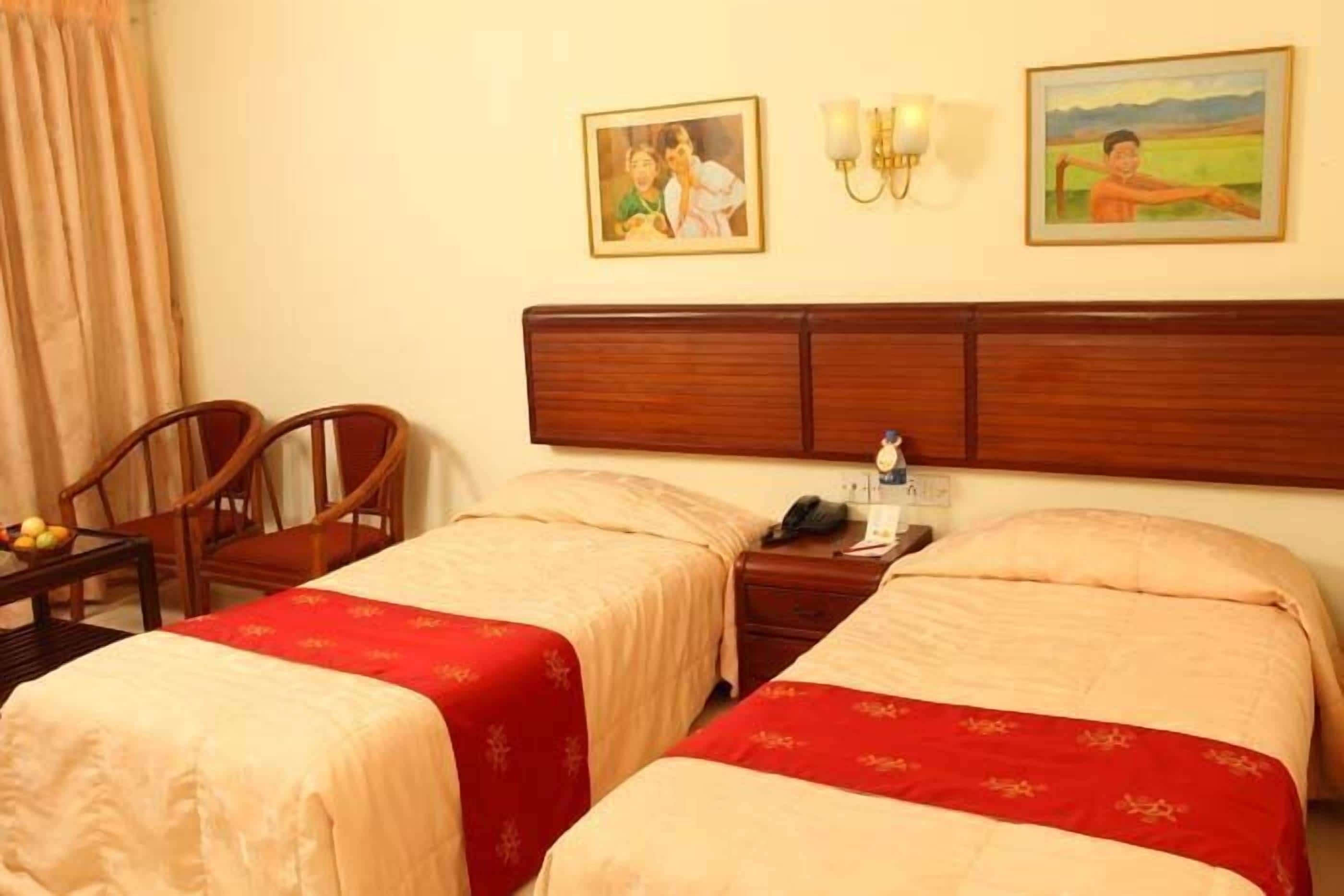 A hotel room with two beds, a wooden headboard, a nightstand with a phone, and two chairs.