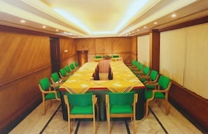 Uma sala de conferências com uma mesa comprida, cadeiras verdes e painéis de madeira.