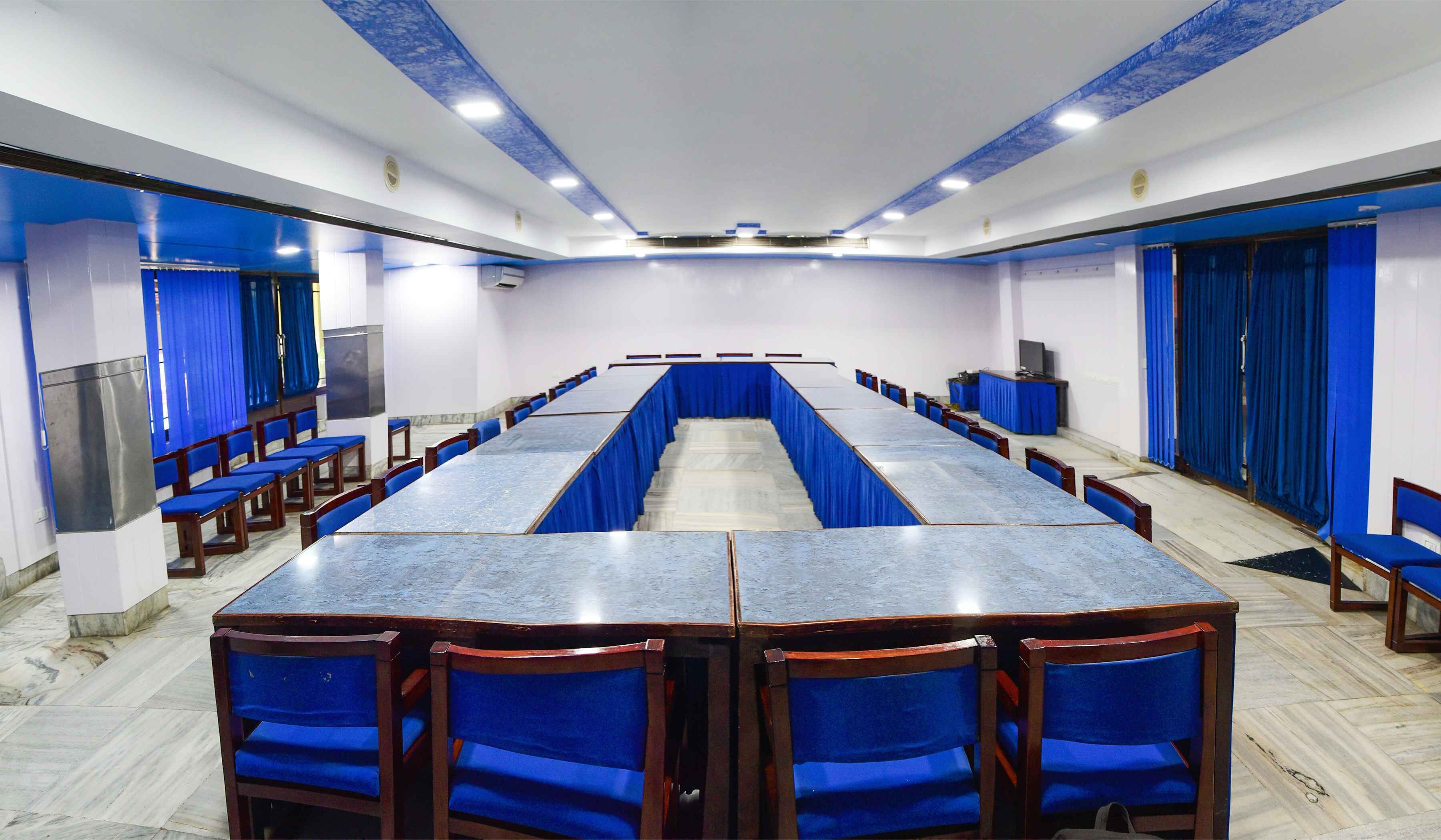 A conference room with a long table and chairs, blue curtains, and a white ceiling with blue accents.