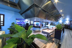 A modern restaurant with a high ceiling, large windows, and indoor plants. - Bharat Hotel (Kanayannur)