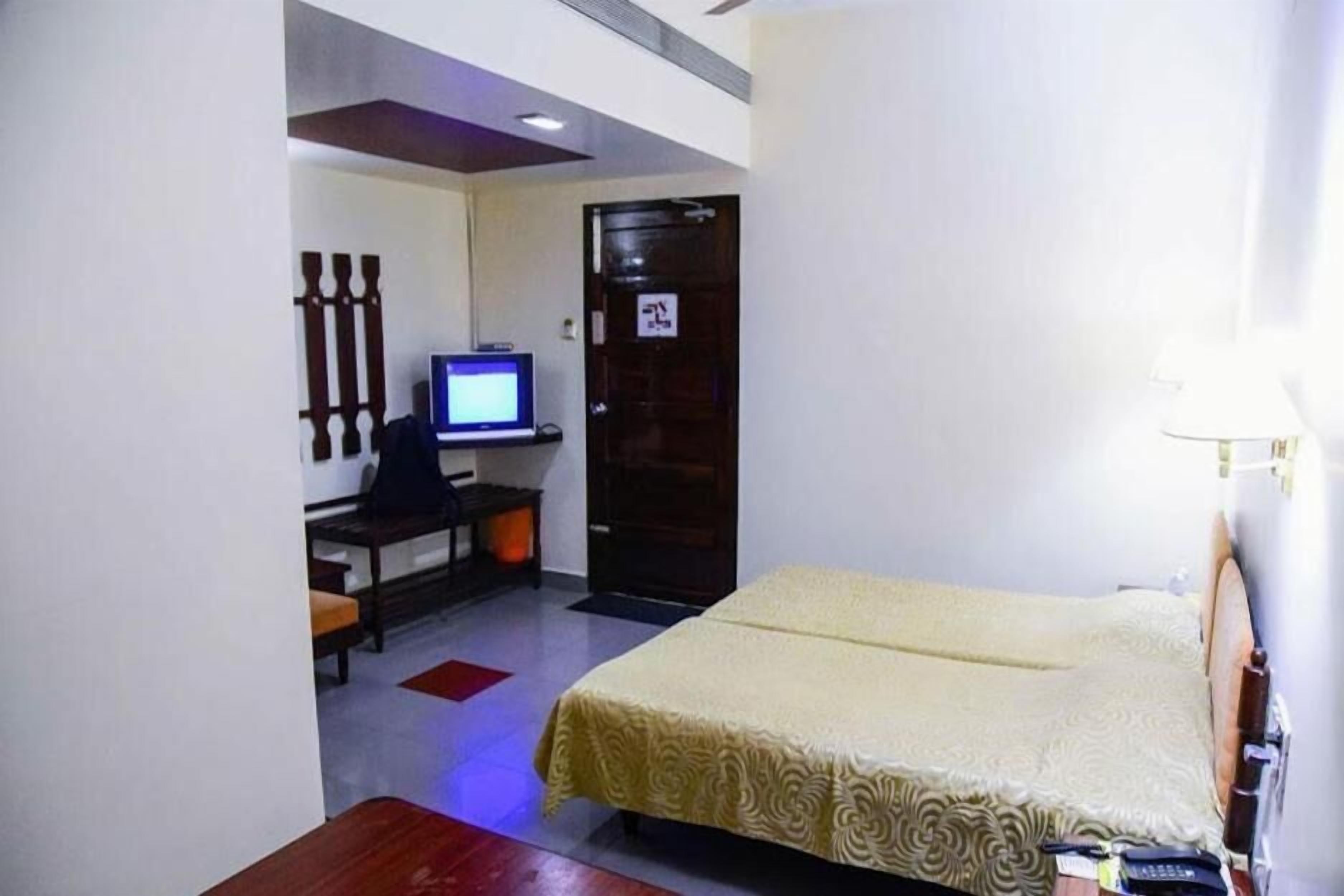 A hotel room with a bed, a desk with a computer, a television, and a door with a sign.