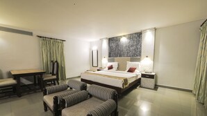 A hotel room with a bed, two armchairs, a small table, and a nightstand with a lamp. - Bharat Hotel (Kanayannur)