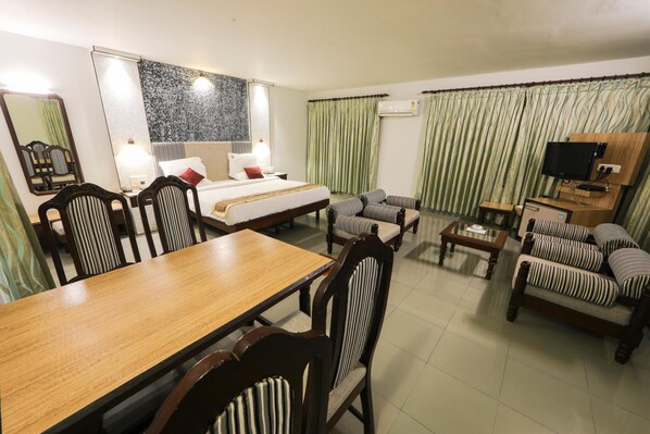 A hotel room with a bed, a dining table, a sofa, and a TV.